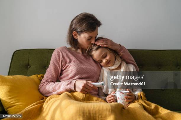 mother embracing sick daughter at home - malattia foto e immagini stock