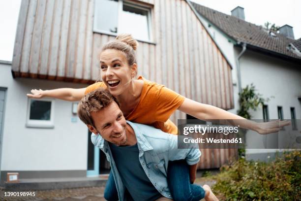 happy man giving piggyback ride to woman with arms outstretched enjoying at backyard - 飛行機のまね ストックフォトと画像