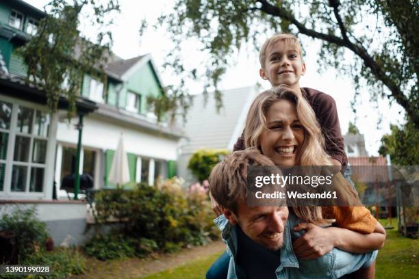 man giving piggyback ride to son and woman enjoying at backyard - vater mutter kind stock-fotos und bilder