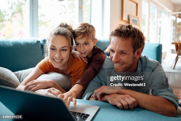 happy mother and father with son watching video on laptop at home - family laptop stock pictures, royalty-free photos & images