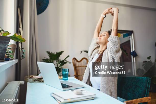freelancer with eyes closed stretching arms sitting at desk - esticar imagens e fotografias de stock