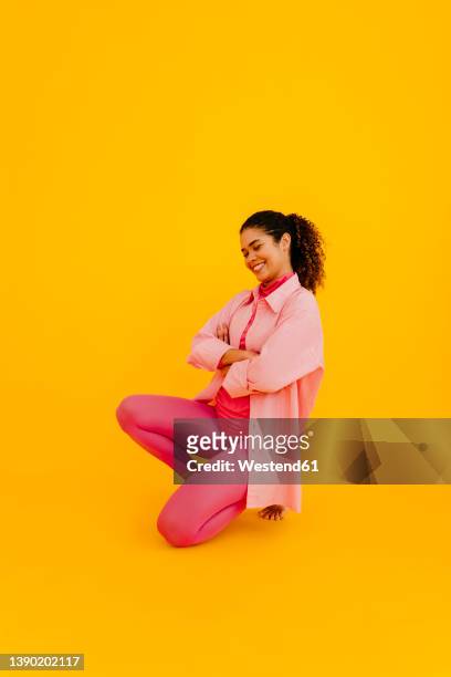 smiling young woman with arms crossed against yellow background - woman kneeling stock-fotos und bilder