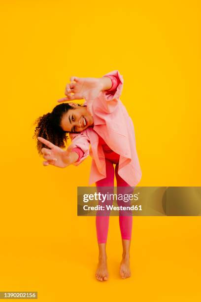 happy young woman gesturing finger frame against yellow background - vornüber beugen stock-fotos und bilder