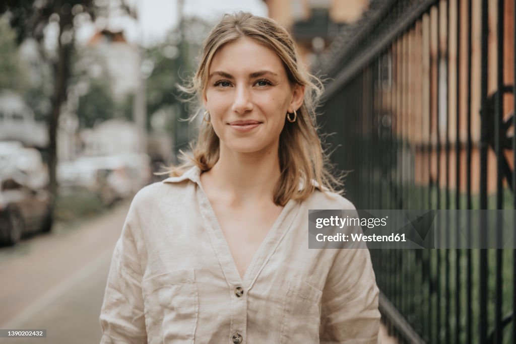 Smiling young woman with blond hair standing on footpath