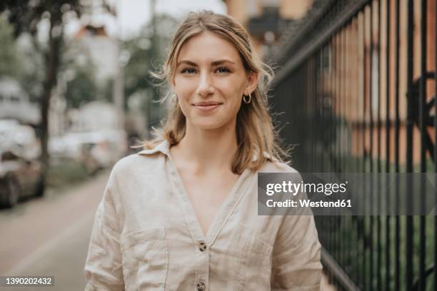 smiling young woman with blond hair standing on footpath - one young woman only foto e immagini stock