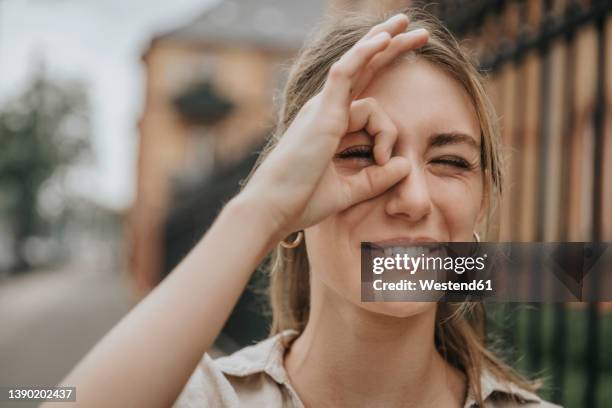 smiling young woman winking eye gesturing ok sign - gesturing ok stock pictures, royalty-free photos & images