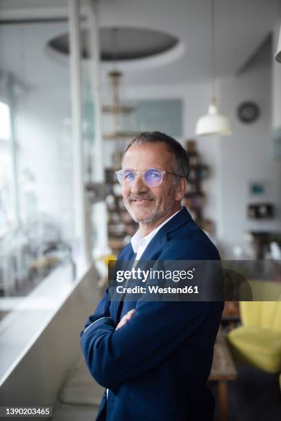 smiling businessman wearing eyeglasses standing with arms crossed in cafe - 60 64 ans photos et images de collection