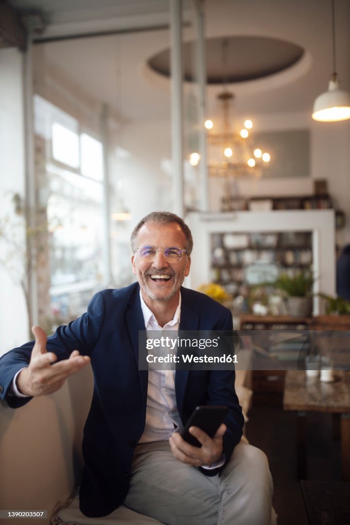 Cheerful businessman with smart phone gesturing with hand