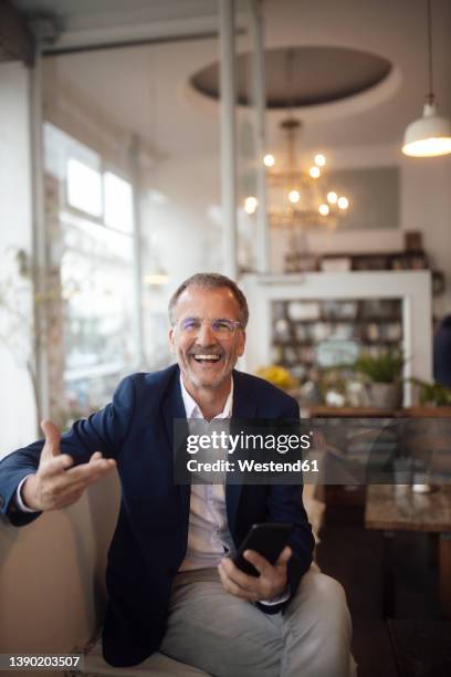 cheerful businessman with smart phone gesturing with hand - business man laughing stock-fotos und bilder