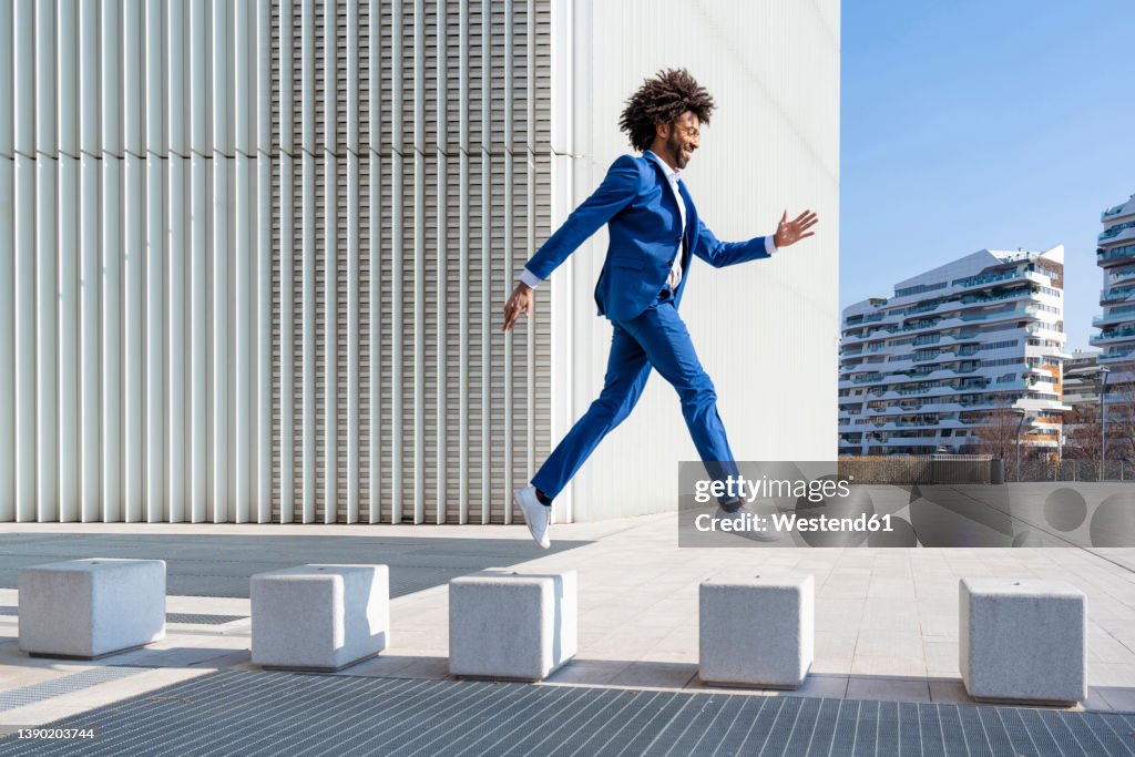Playful businessman jumping on concrete block