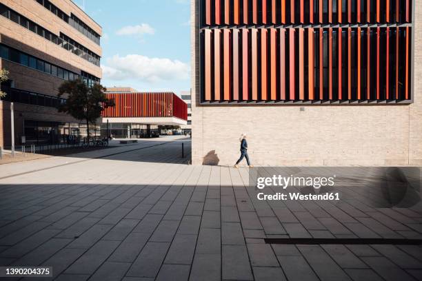 businesswoman walking outside office building on sunny day - kantoorpark stockfoto's en -beelden