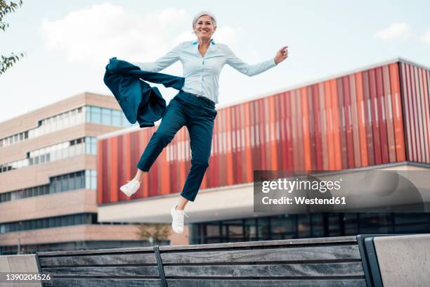 happy businesswoman with blazer jumping at office park - woman jumping happy stockfoto's en -beelden
