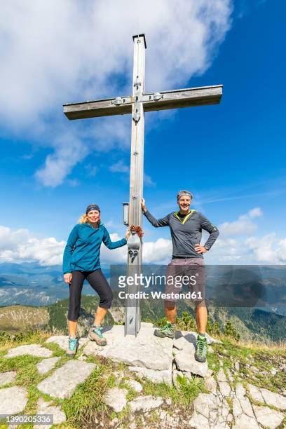 two hikers posing by summit cross of demeljoch mountain - gipfelkreuz stock-fotos und bilder