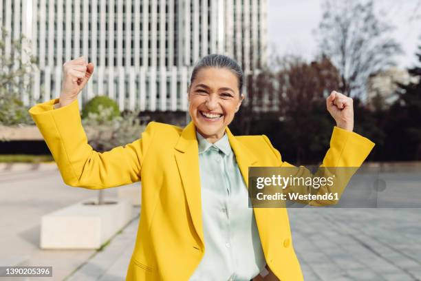 cheerful businesswoman flexing muscles at office park on sunny day - flexionar los músculos fotografías e imágenes de stock