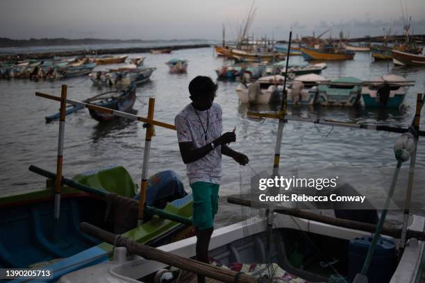 Fisherman Lassantha Kumar repairs a fishing net on a boat in a harbour on April 05, 2022 in Dikwella, Sri Lanka. Local fishermen say the country’s...