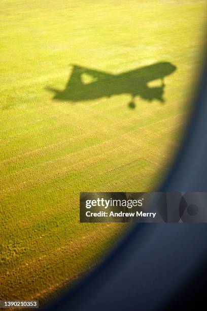 airplane shadow landing at airport, passenger window view, runway green grass area - landing gear stock-fotos und bilder
