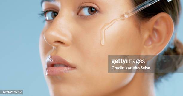 studio shot of a beautiful young woman applying face serum against a blue background - applying stockfoto's en -beelden