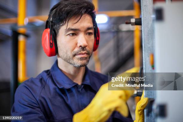 retrato de un trabajador industrial asiático-americano medianamente adulto con orejeras - orejeras fotografías e imágenes de stock