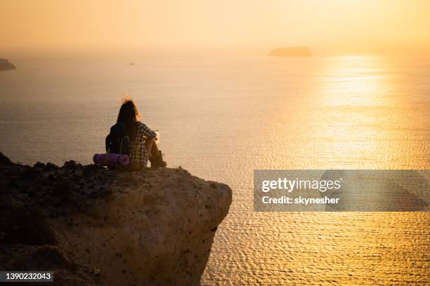 back view of a female backpacker resting on water break above the sea. - carefree beach stock pictures, royalty-free photos & images