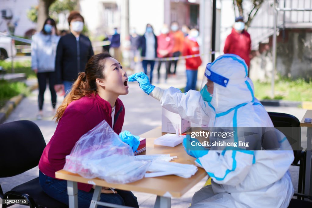 En avril 2022, un travailleur médical portant des vêtements de protection effectuait des tests et des prélèvements d’acides nucléiques pour une femme à Shanghai, en Chine.