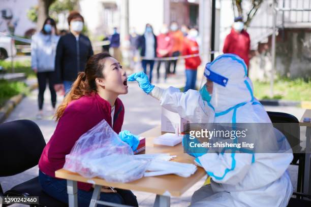in april 2022, a medical worker wearing protective clothing was conducting nucleic acid testing and sampling for a woman in shanghai, china - china coronavirus stock pictures, royalty-free photos & images