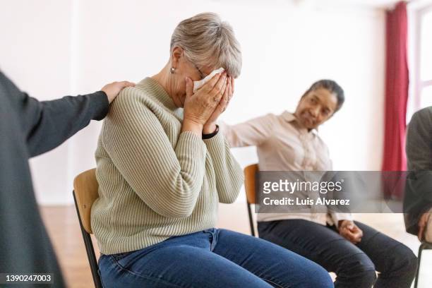 support group consoles a sad woman during a therapy session - old lady crying out for help stock pictures, royalty-free photos & images