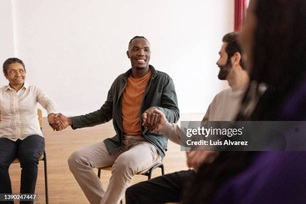 happy people holding hands while sitting in a circle during group therapy session - prayer circle stock pictures, royalty-free photos & images