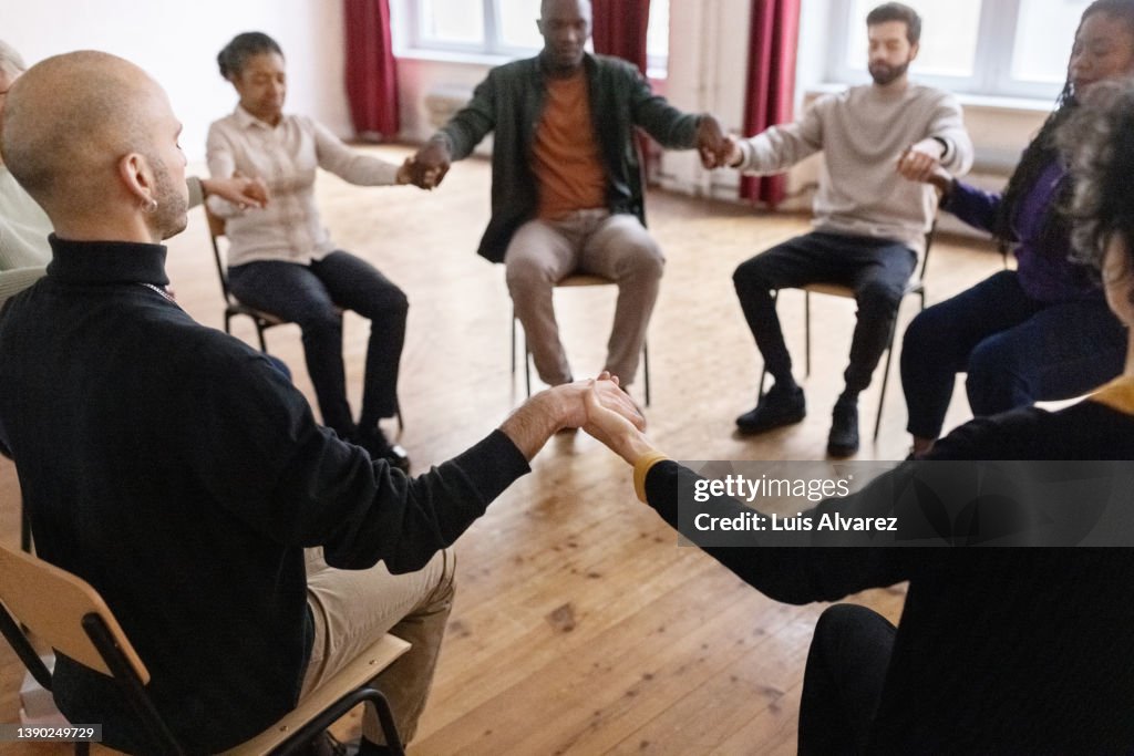 Support group sitting in a circle holding hands