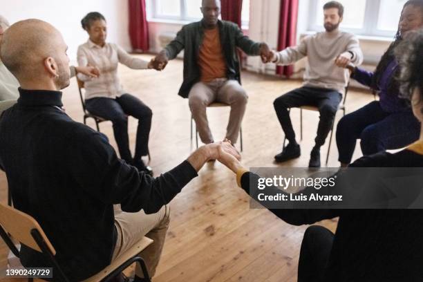 support group sitting in a circle holding hands - aa meeting stock pictures, royalty-free photos & images