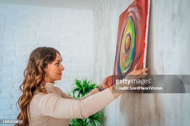 woman hanging picture on wall - hanging art stock pictures, royalty-free photos & images