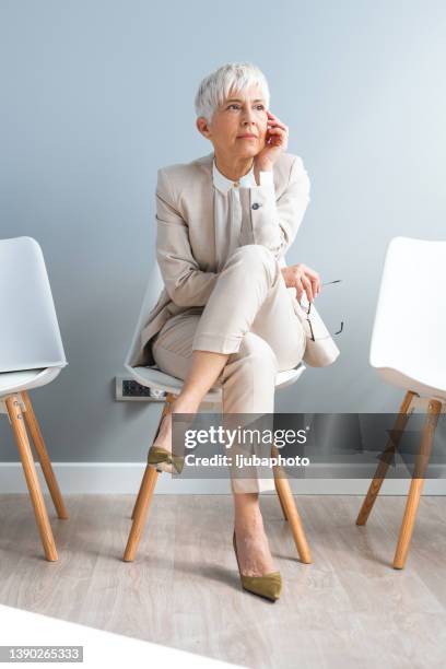 businesswoman looking thoughtful while waiting in line against a grey background - lounge chair bildbanksfoton och bilder