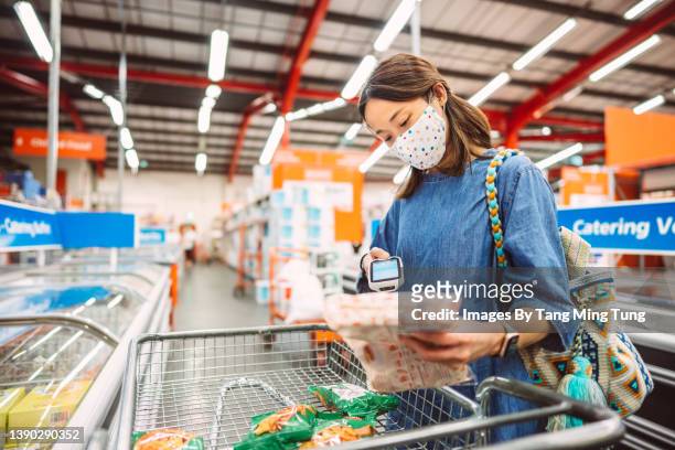 young asian woman in protective face mask using handheld barcode reader while shopping in supermarket - scanner stock stock pictures, royalty-free photos & images