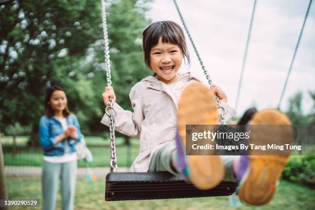lovely little girl playing joyfully on a swing set in playground - andar de baloiço imagens e fotografias de stock