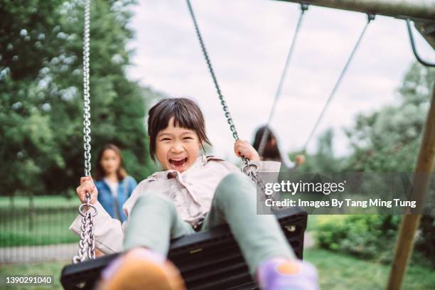 lovely little girl smiling at the camera while playing on a swing set in playground joyfully - amusement park stock-fotos und bilder