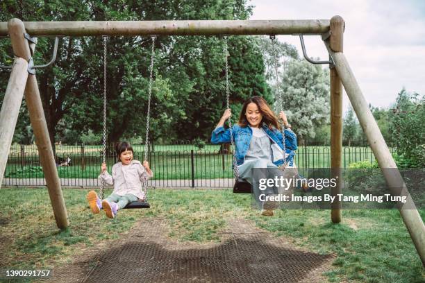 mom & daughter having fun playing on swing set together in public park - swing stock pictures, royalty-free photos & images