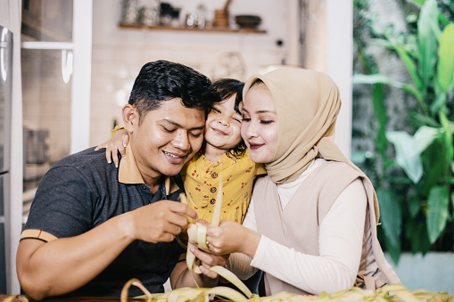 Young Indonesian family, preparing food of ketupat, for celebrating Eid Al-Fitr at home