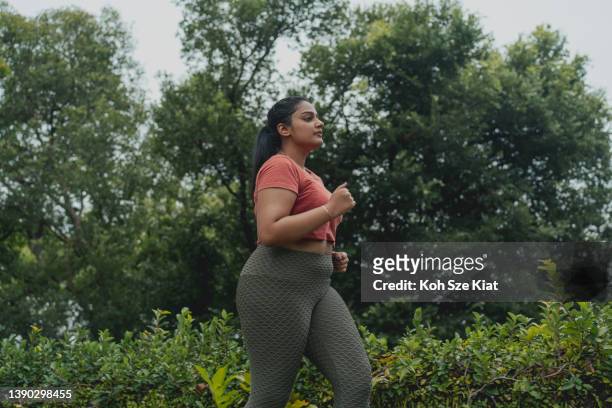 asiatisch-indische körperpositive frau, die in einem outdoor-park joggt - fat asian woman stock-fotos und bilder