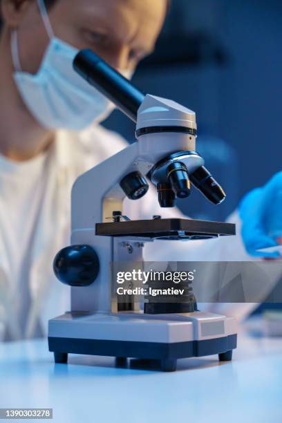 a microscope in the foreground and a scientist in the background in professional light - doctor looking away stock pictures, royalty-free photos & images