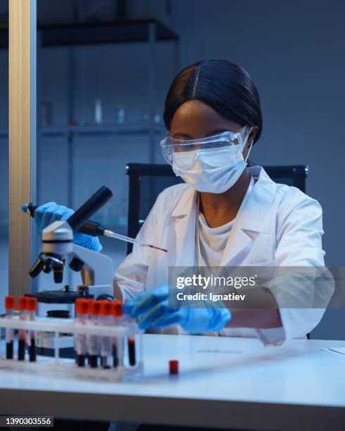 the process of blood analysis. a young african-american lab assistant working with blood samples in test tubes - virology stockfoto's en -beelden