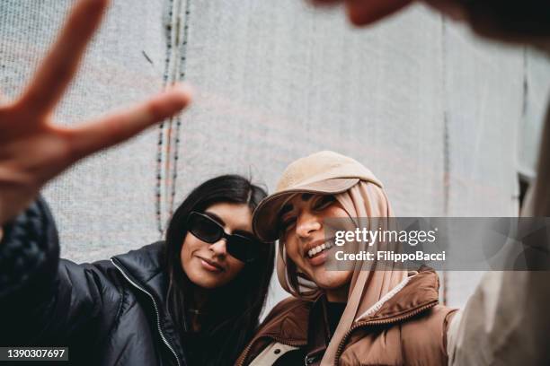 two young adult girls are making funny gestures to the camera - young muslim stockfoto's en -beelden