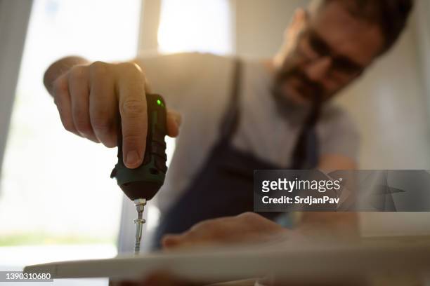 carpenter with electric screwdriver connecting pieces of furniture in the kitchen - electric screwdriver stock pictures, royalty-free photos & images