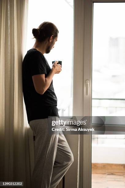 man with coffee cup looking through window - jogging pants 個照片及圖片檔