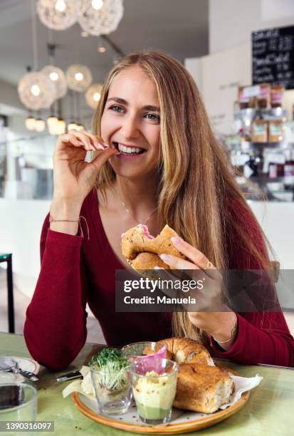 smiling woman enjoying breakfast in restaurant - woman eating bagel stock pictures, royalty-free photos & images