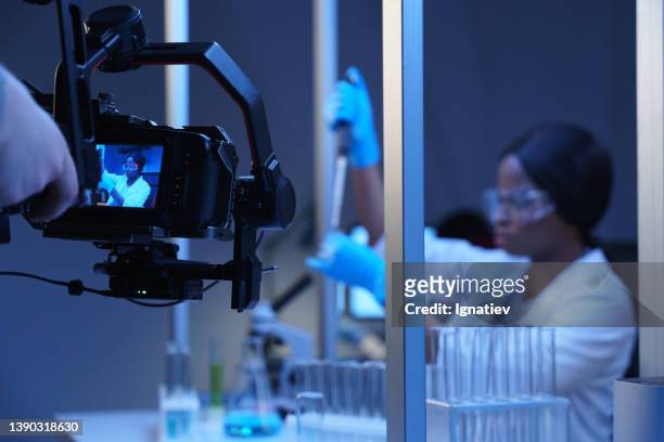una cámara profesional fotografiando a una actriz en el papel de un científico en un laboratorio. backstage de la filmación de una película de una foto ambientada en las decoraciones de un laboratorio - film screening fotografías e imágenes de stock