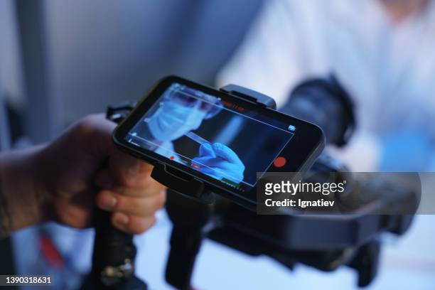 a hand of an operator with a shooting camera and a smart phone screen, showing an image from the camera, where we see a man in a protective mask - camera operator imagens e fotografias de stock