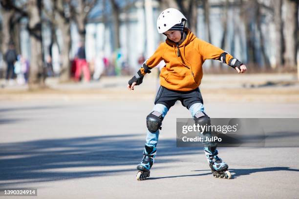 little boy roller skating in public park in helmet and body protection - skaten stockfoto's en -beelden