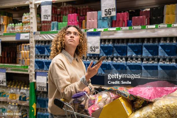 young woman looking up in shopping aisle whilst holding her phone - beautiful plump women fotografías e imágenes de stock