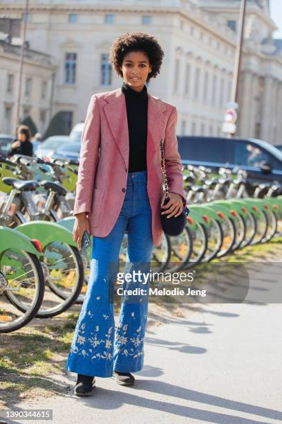 Angolan model Blesnya Minher wears a pink blazer, black turtleneck, blue flare jeans with floral embroidery, black quilted Chanel purse, and black...