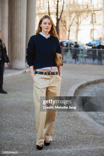 French-American model Camille Rowe wears a blue sweater over a white shirt, small brown Miu Miu purse, low-rise Miu Miu khaki pants, belt, and...