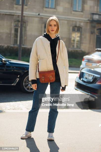 Dutch model Puck Schrover wears a white quilted jacket, black hoodie, brown leather camera bag, black jeans, and white Converse sneakers after the...